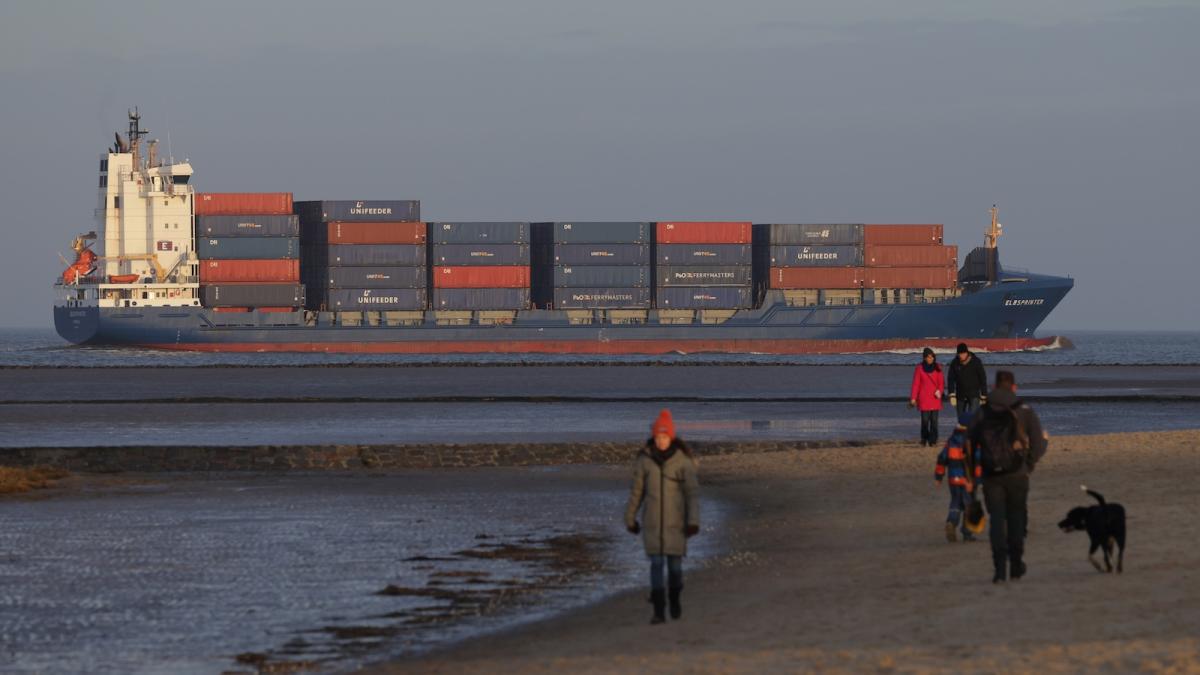 A large freight ship in background, with people walking on the beach in foreground, with hazy air.