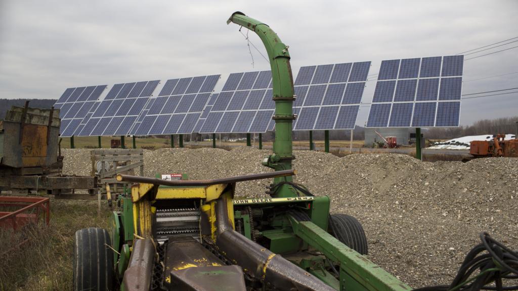 Farm equipment in front of a raised bed of dirt with solar panels in the background.