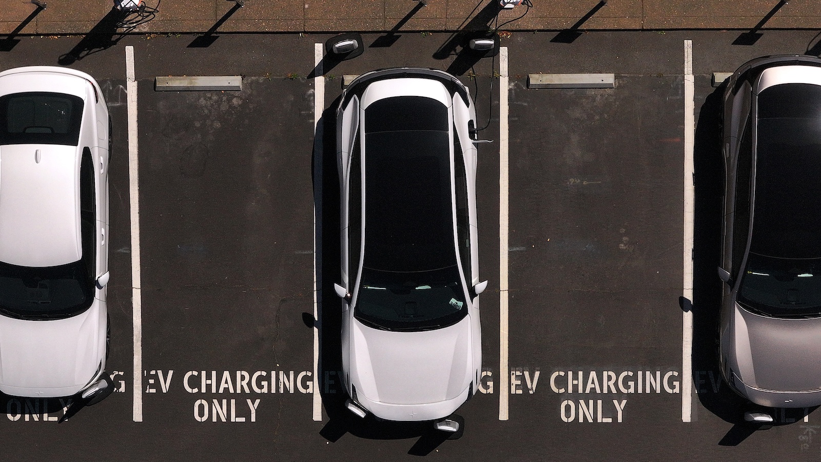 Aerial view of a parking lot with three cars parked. In between them are empty parking spaces with the text "EV charging only" painted in white.