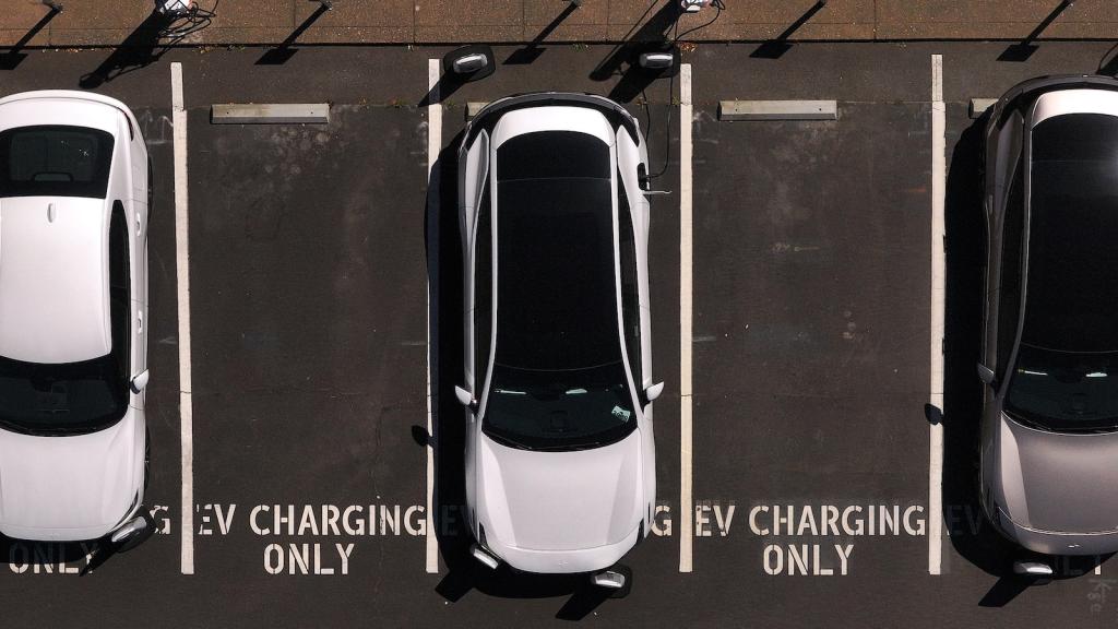 Aerial view of a parking lot with three cars parked. In between them are empty parking spaces with the text 