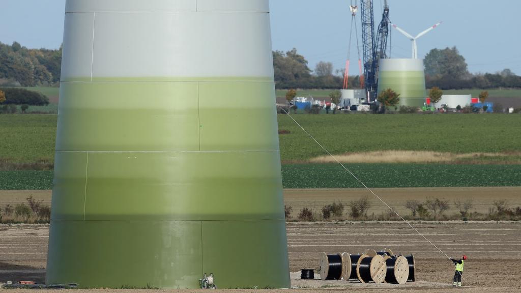 A worker pulls on a rope to secure equipment at a wind turbine under construction at the Werder/Kassin RH2-WKA windpark in Germany. Another turbine rises in the background.