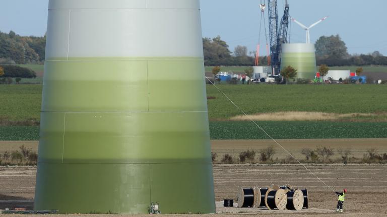 A worker pulls on a rope to secure equipment at a wind turbine under construction at the Werder/Kassin RH2-WKA windpark in Germany. Another turbine rises in the background.