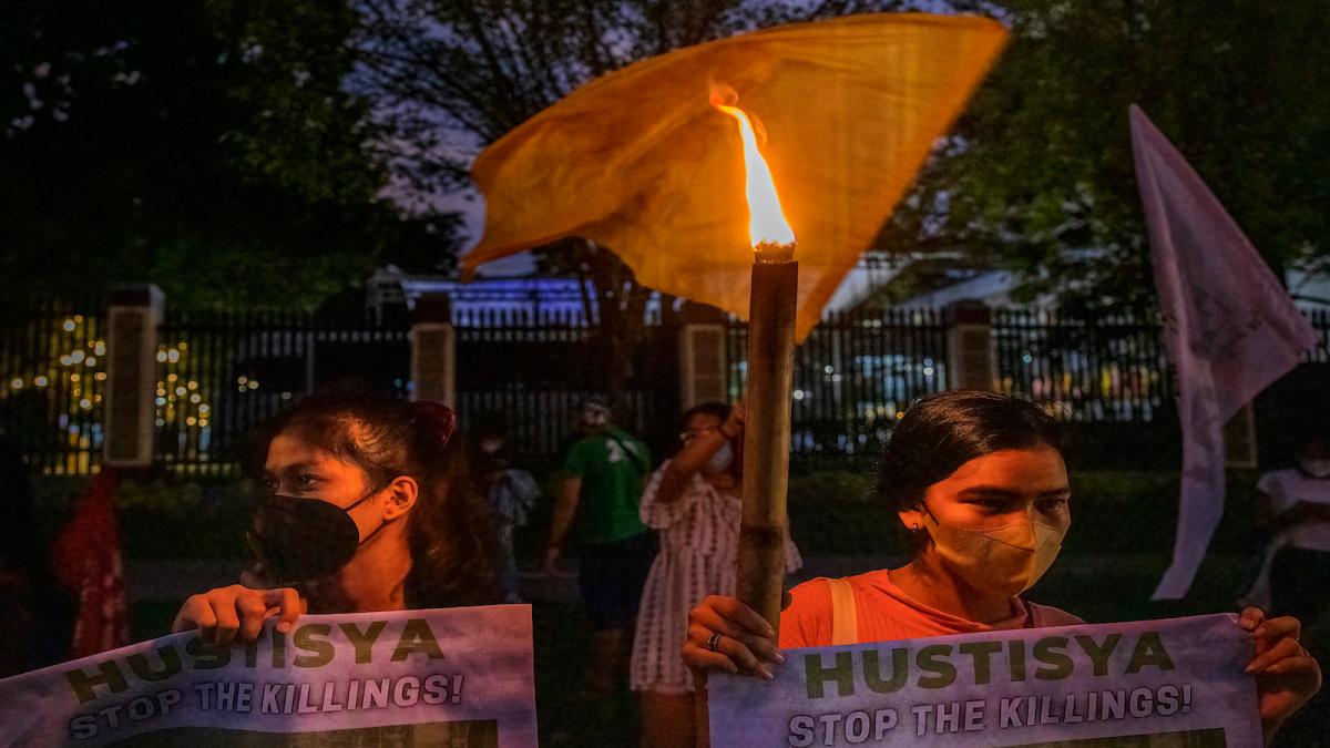 two protestors hold up signs and a torch at a rally