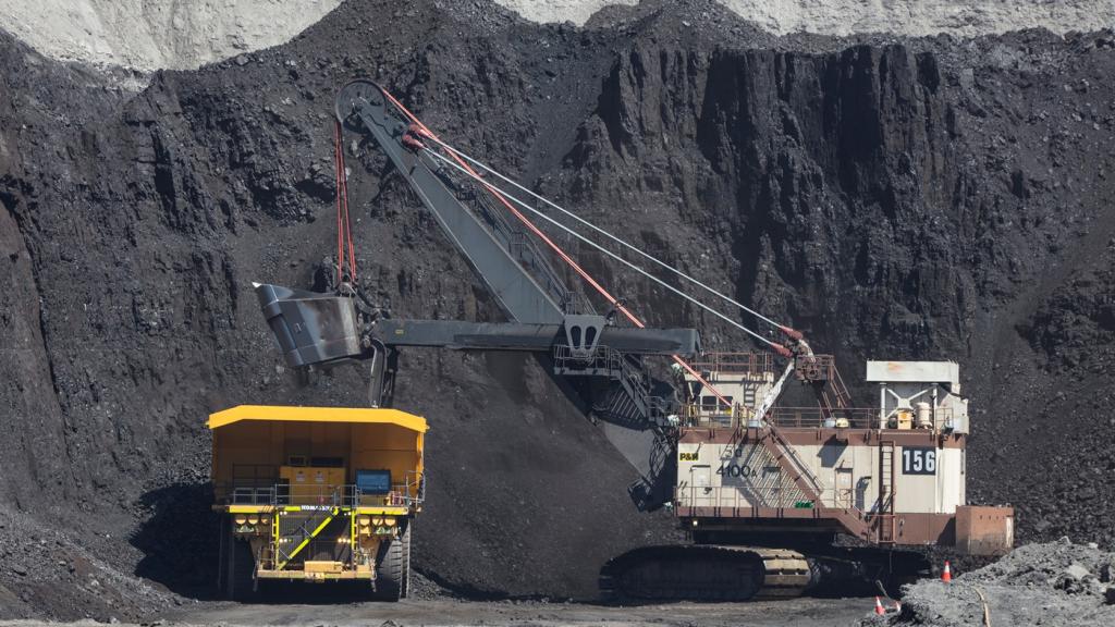 A yellow vehicle and a construction vehicle sit in front of a mound of coal