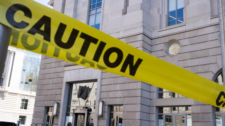 A yellow caution tape is draped in front of a white and gray building