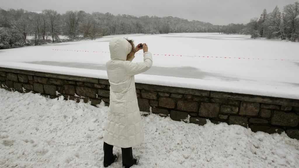 A woman in a white puffy coat taking a picture of a frozen lake