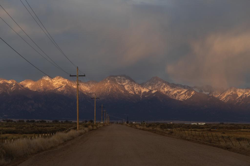 A desolate highway in Colorado, with transmission lines in the foreground and mountains in the background