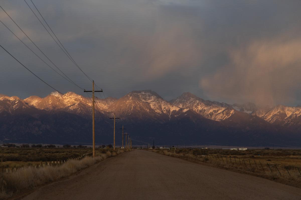 A desolate highway in Colorado, with transmission lines in the foreground and mountains in the background