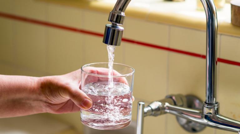 Hand holding a cup as water from a faucet fills the cup.