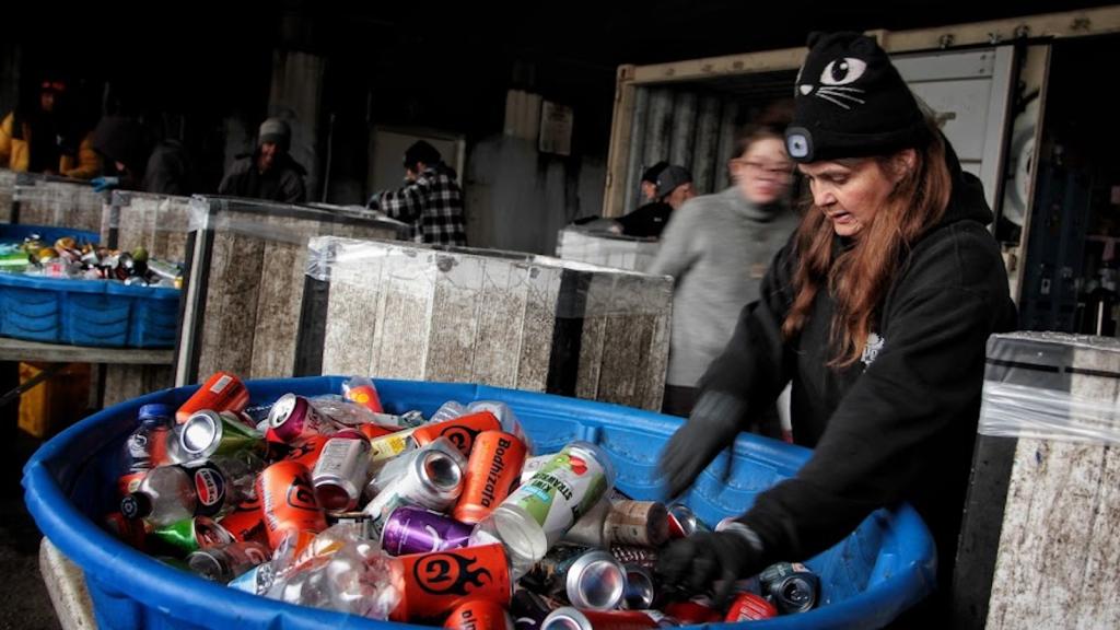 A worker sifts through cans in a blue tub