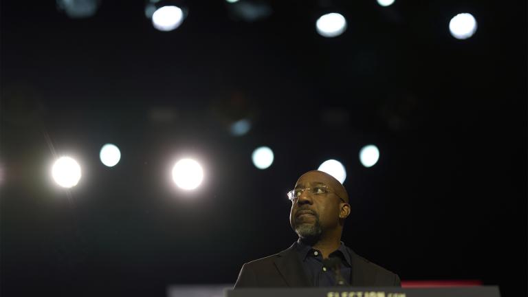 Senator Raphael Warnock at a podium against a dark background with blurred lights