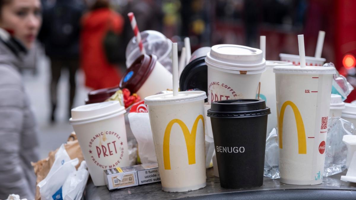 Empty to-go cups piled on top of a trash can