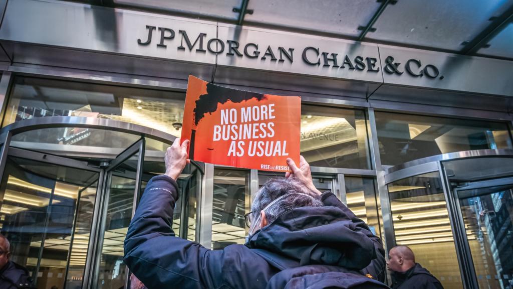 A man holds a sign that says no more business as usual in front of JP Morgan Chase
