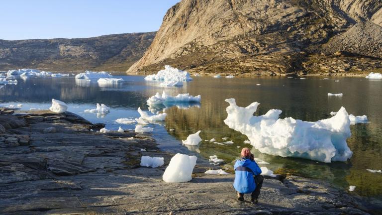 a man crouches on a rock in front of pieces of a glacier, which are drifting out to sea
