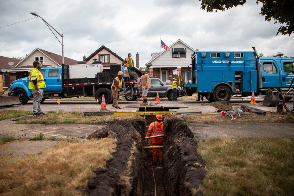 People dig a trench to replace lead pipes in front of a house