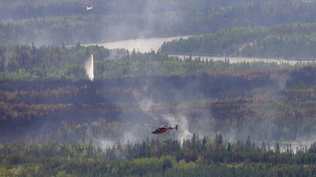 Helicopter and airplane flying above wildfire smoke