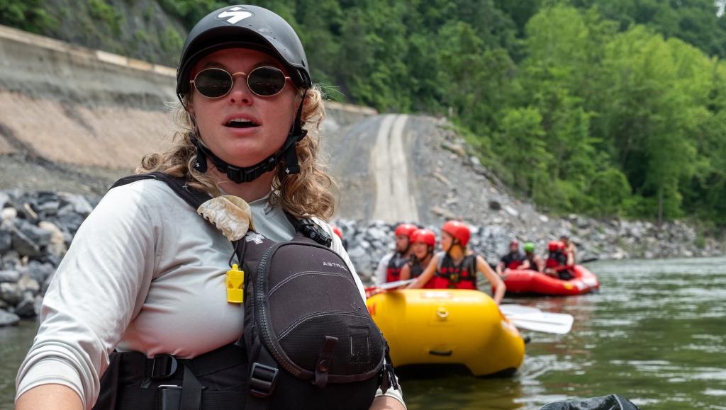 A female river guide leads two groups of rafts down a river