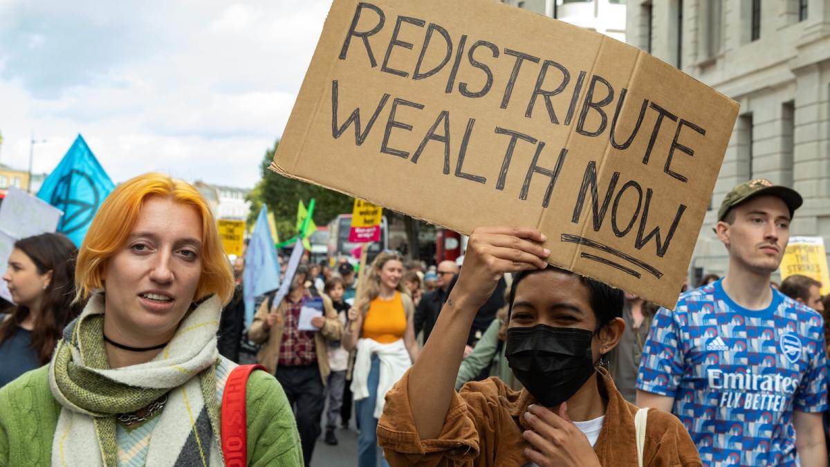 Climate activists, one of whom is carrying a picket reading, "Redistribute wealth now," from the Just Stop Oil coalition march in London in October, 2022.