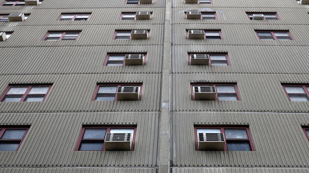 A gray building with windows each with an air conditioner embedded