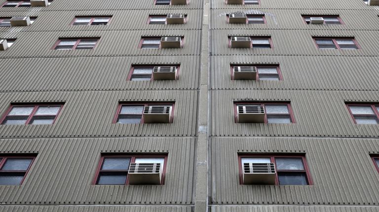 A gray building with windows each with an air conditioner embedded