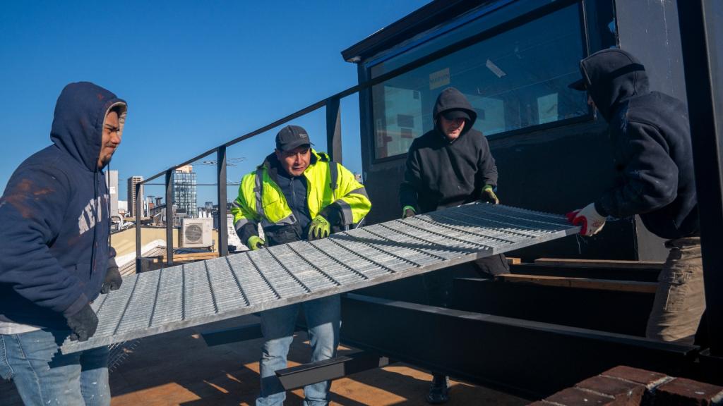 A group of men hold a huge metal grate on top of an apartment building