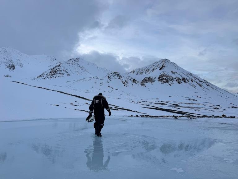 A lone human figure walks on melting ice in the Arctic