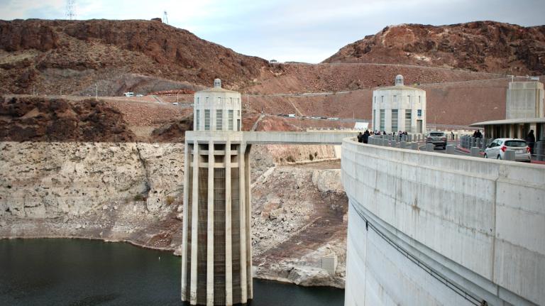 The upper building of a dam sits amid red rocks and a low water level