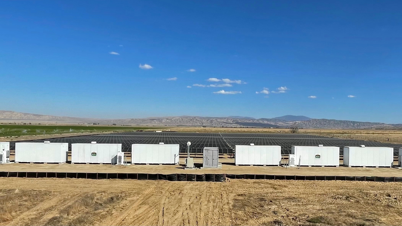An empty field filled with black solar panels surrounded by white trailers