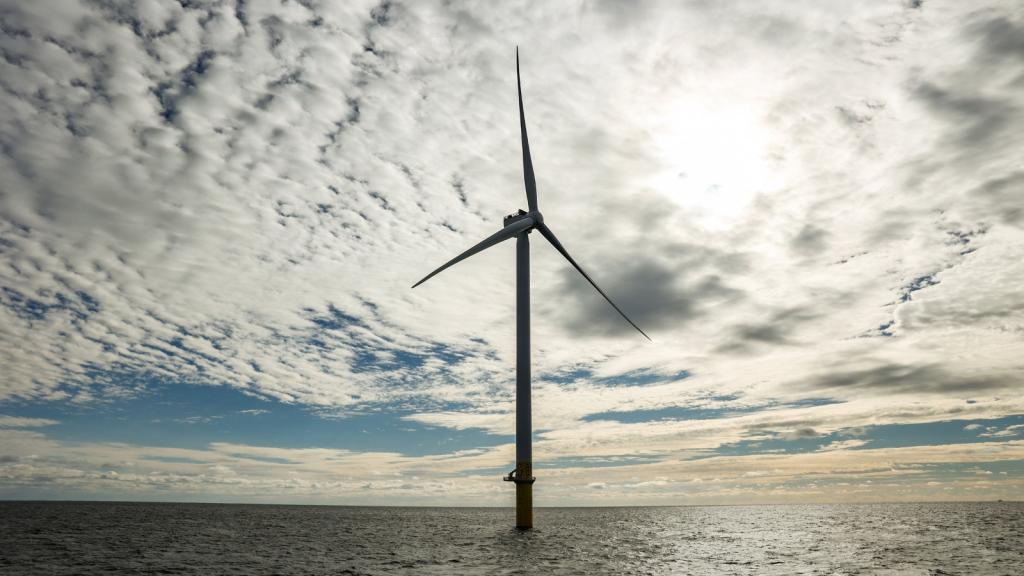 A wind turbine stands in the middle of the ocean under a cloudy sky