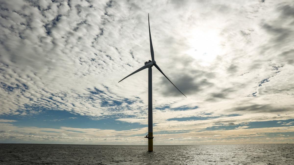 A wind turbine stands in the middle of the ocean under a cloudy sky