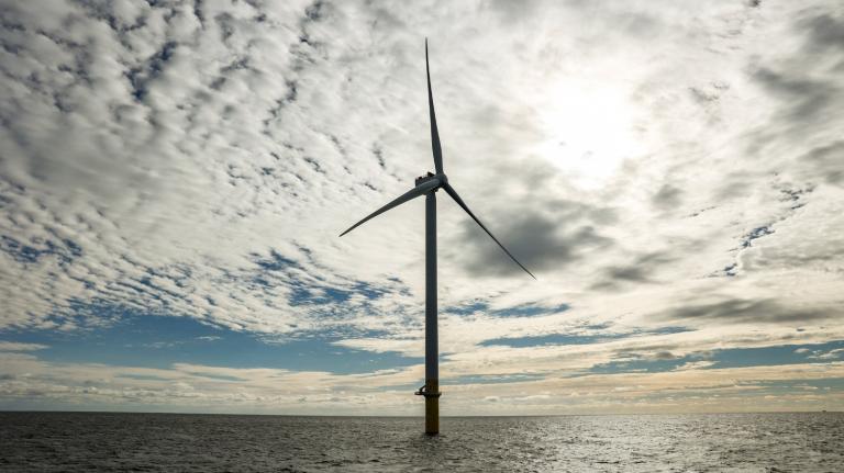 A wind turbine stands in the middle of the ocean under a cloudy sky