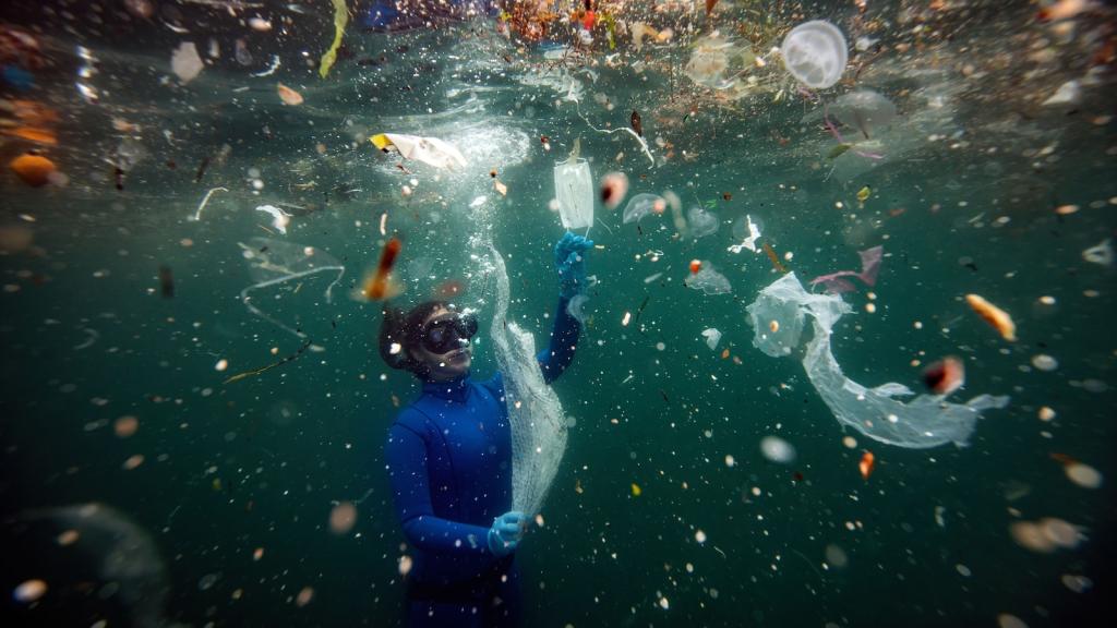 Diver underwater in a blue wetsuit, near the surface, with plastic floating all around them.