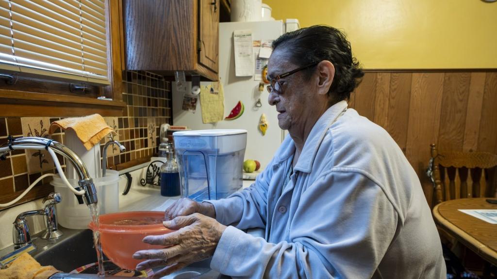 a woman in her 70s filters water at a kitchen sink