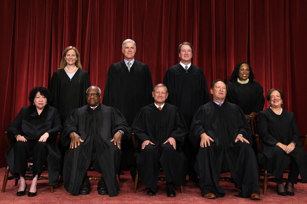 Supreme Court justices pose in two rows, wearing robes, in front of a red curtain.