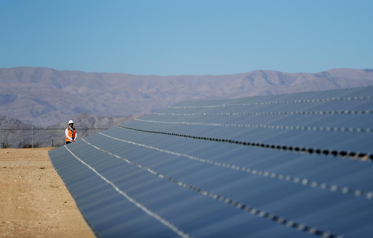 A man in a vest and hard hat stands next to solar panels