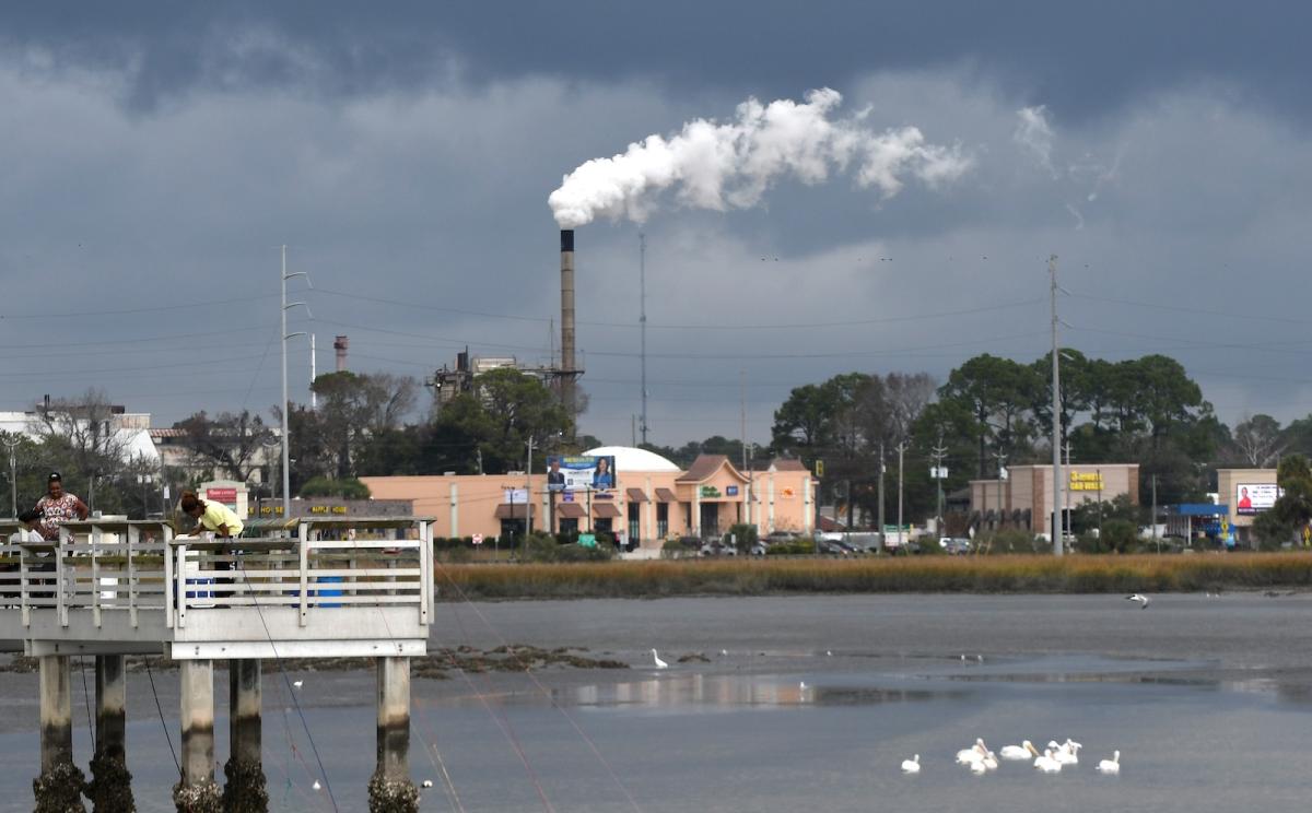A photo shows a billowing smokestack in the background of a small waterfront town