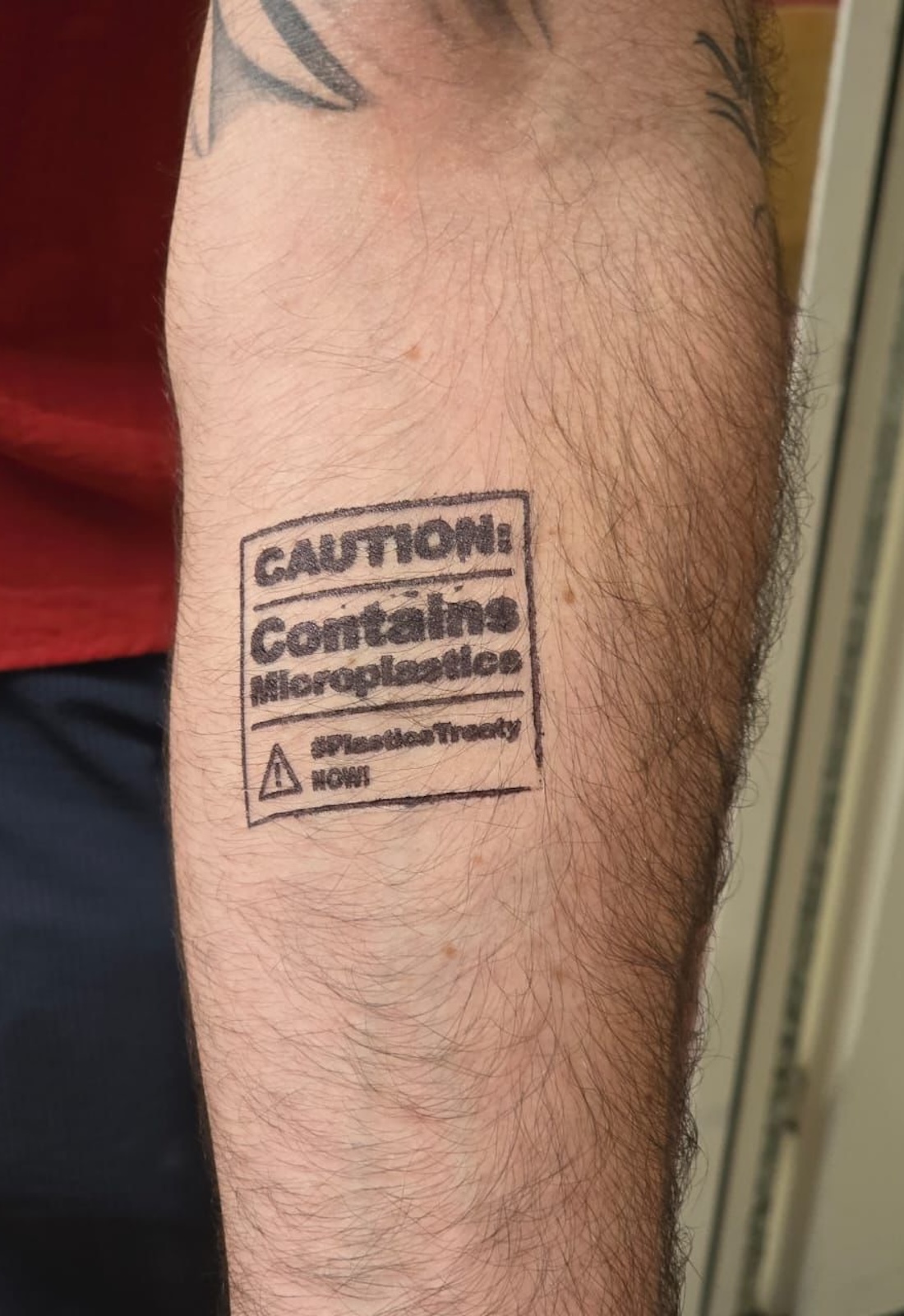 A bare arm with a temporary tattoo saying, "Caution: contains microplastics"