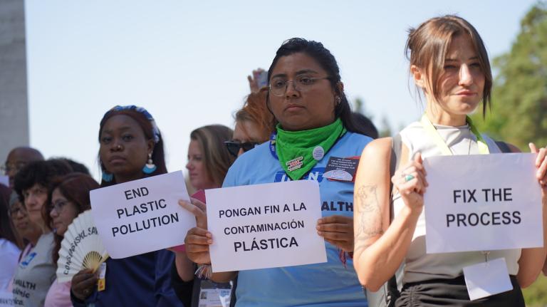 People hold signs protesting plastic pollution. A woman in center has a sign reading 