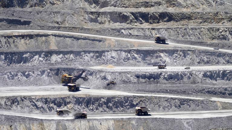 A large open-pit mine with terraced layers with several dump trucks and an excavator