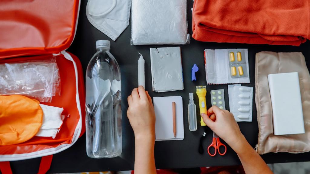 A woman prepares an emergency kit for facing a natural disaster, placing a flashlight, first aid kit, medication, water, and other supplies into a go-bag.