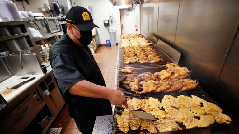 a fast-food worker tends to chicken pieces roasting on a grill in an El Pollo Loco restaurant