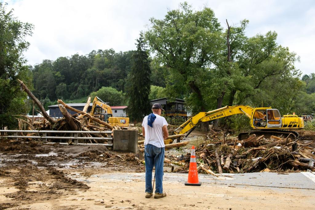 A man views the removal of debris in a storm-damaged neighborhood