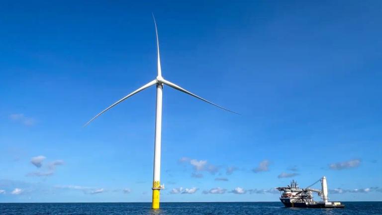 A white wind turbine stands in the middle of the ocean