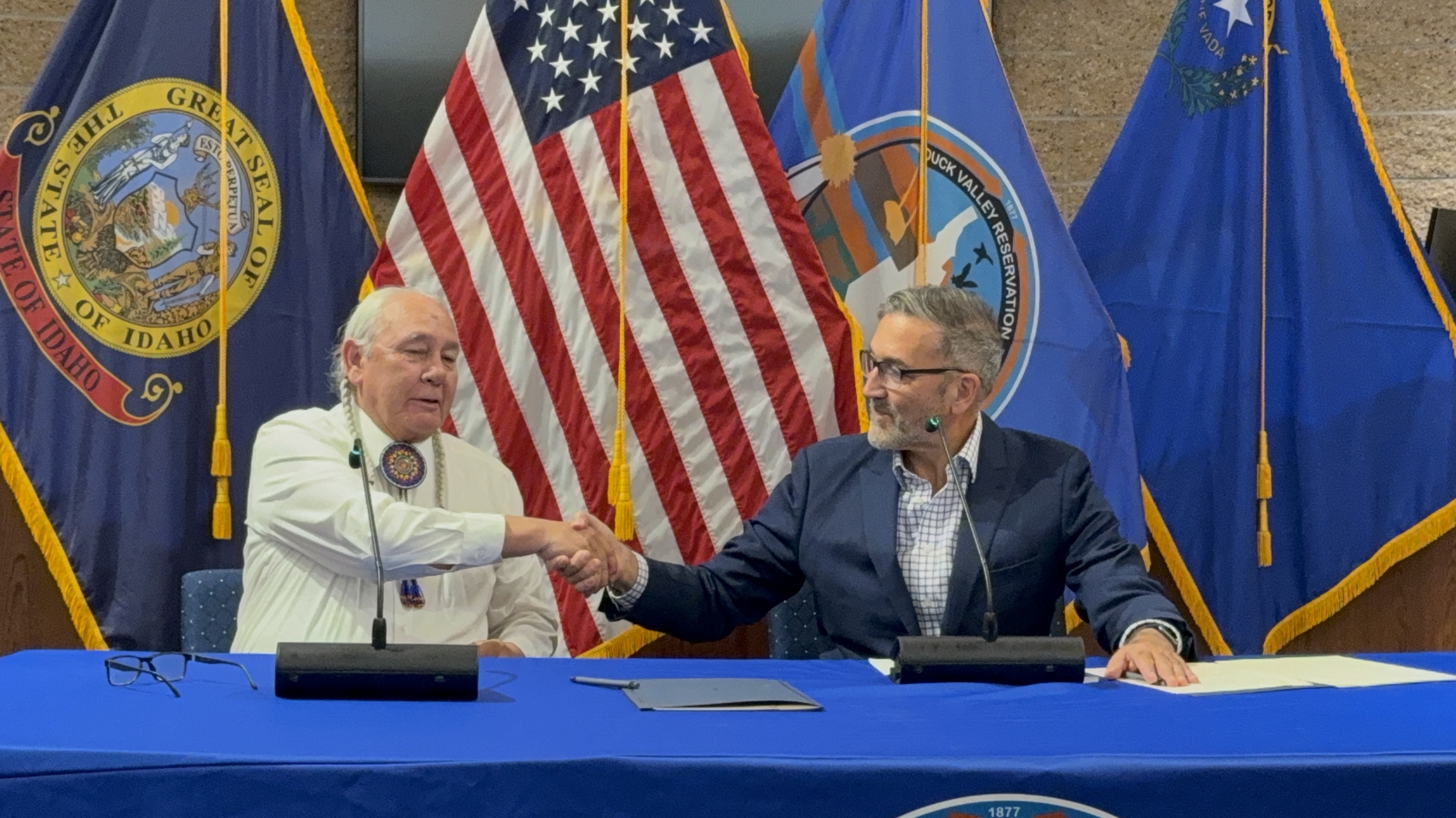 Two men shaking hands in front of flags
