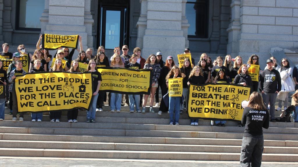Teenagers with yellow signs rally outside of a white building