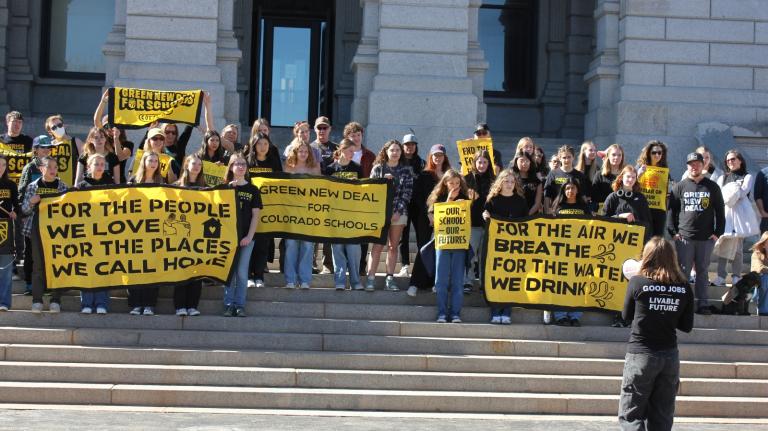 Teenagers with yellow signs rally outside of a white building