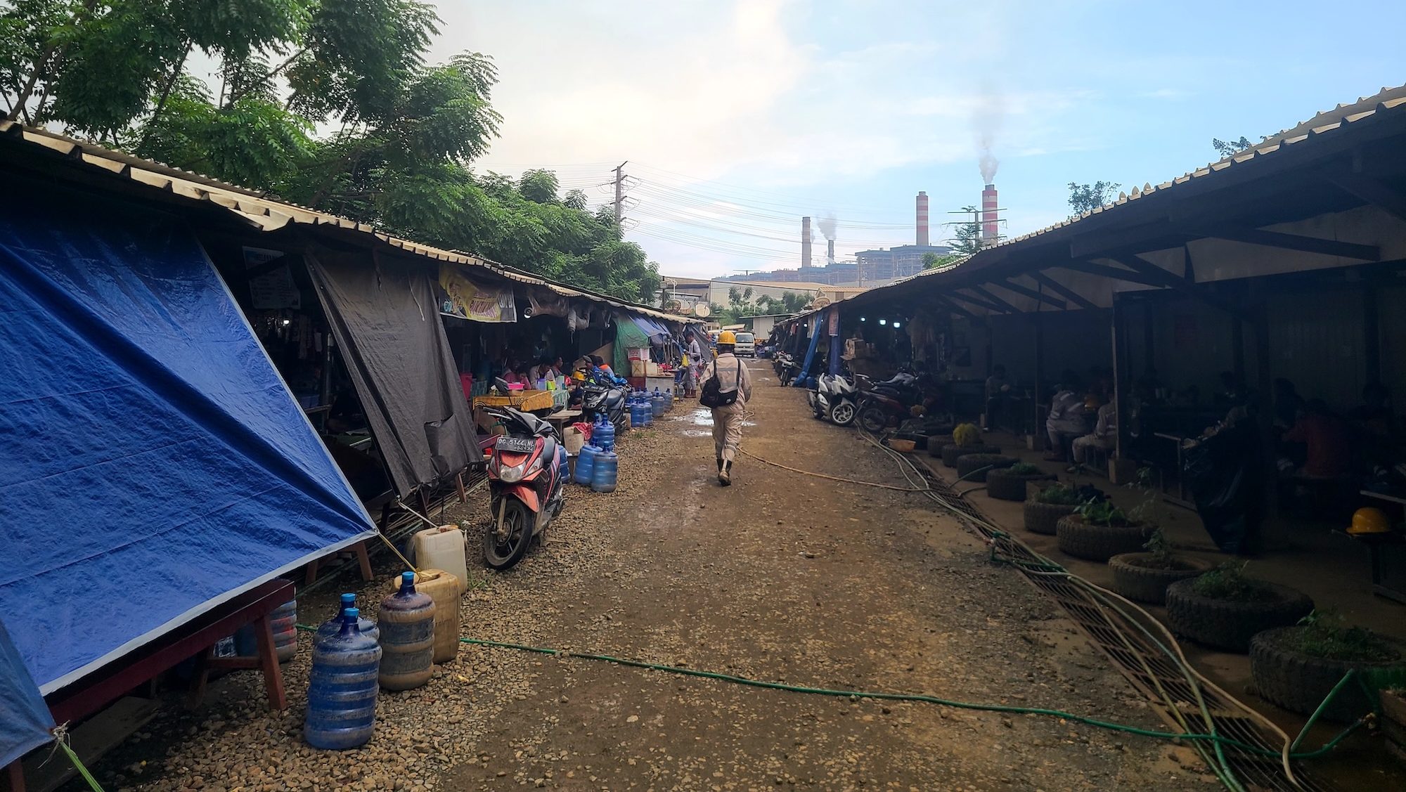 a worker walks through a row of stalls toward an industrial plant