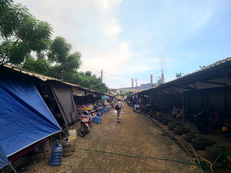a worker walks through a row of stalls toward an industrial plant