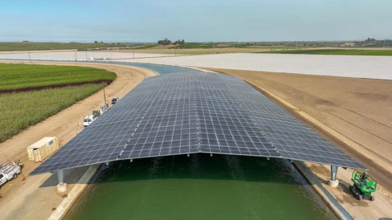An aerial view of a canal cutting through agricultural fields with huge black solar panels stretched over it