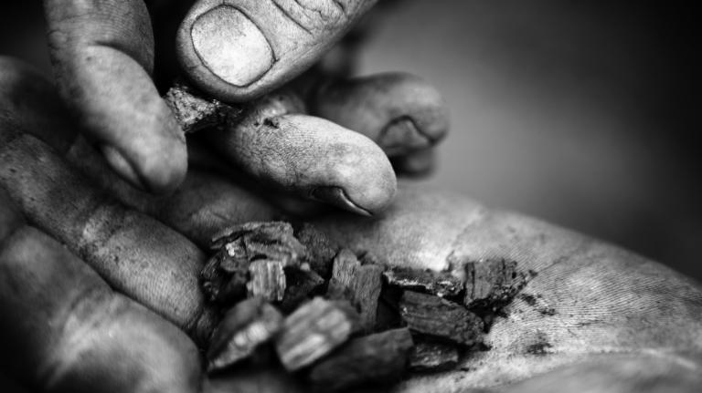 A farmer holds a handful of biochar in his soot-covered hands.